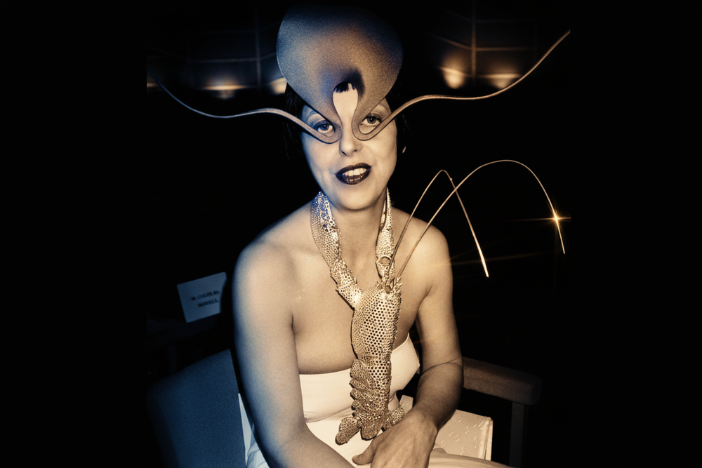 Isabella Blow wearing a dramatic sculptural Philip Treacy hat and crystal-embellished gloves, photographed in striking black and white with cinematic lighting - the iconic British fashion editor and muse who discovered Alexander McQueen