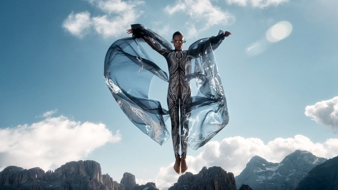 Iris van Herpen Earthrise couture look featuring a futuristic bodysuit with flowing translucent wings floating above a mountain landscape
