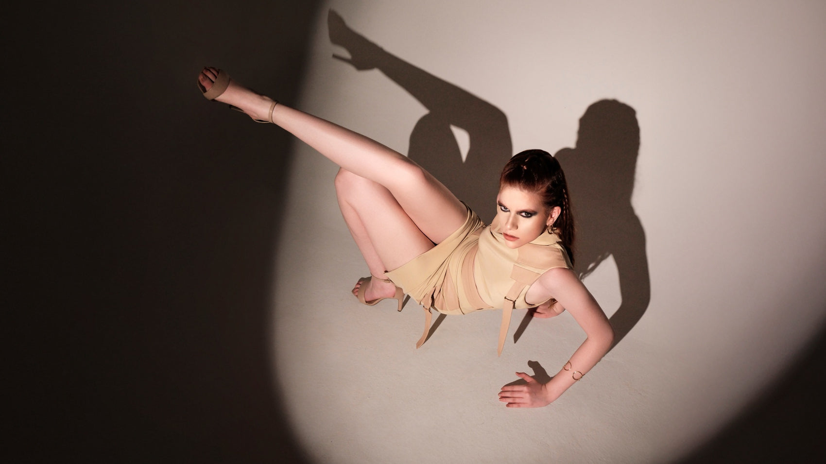 Model in beige skirt set striking an avant-garde pose with extended leg and bold shadows, high-fashion black and white editorial look.