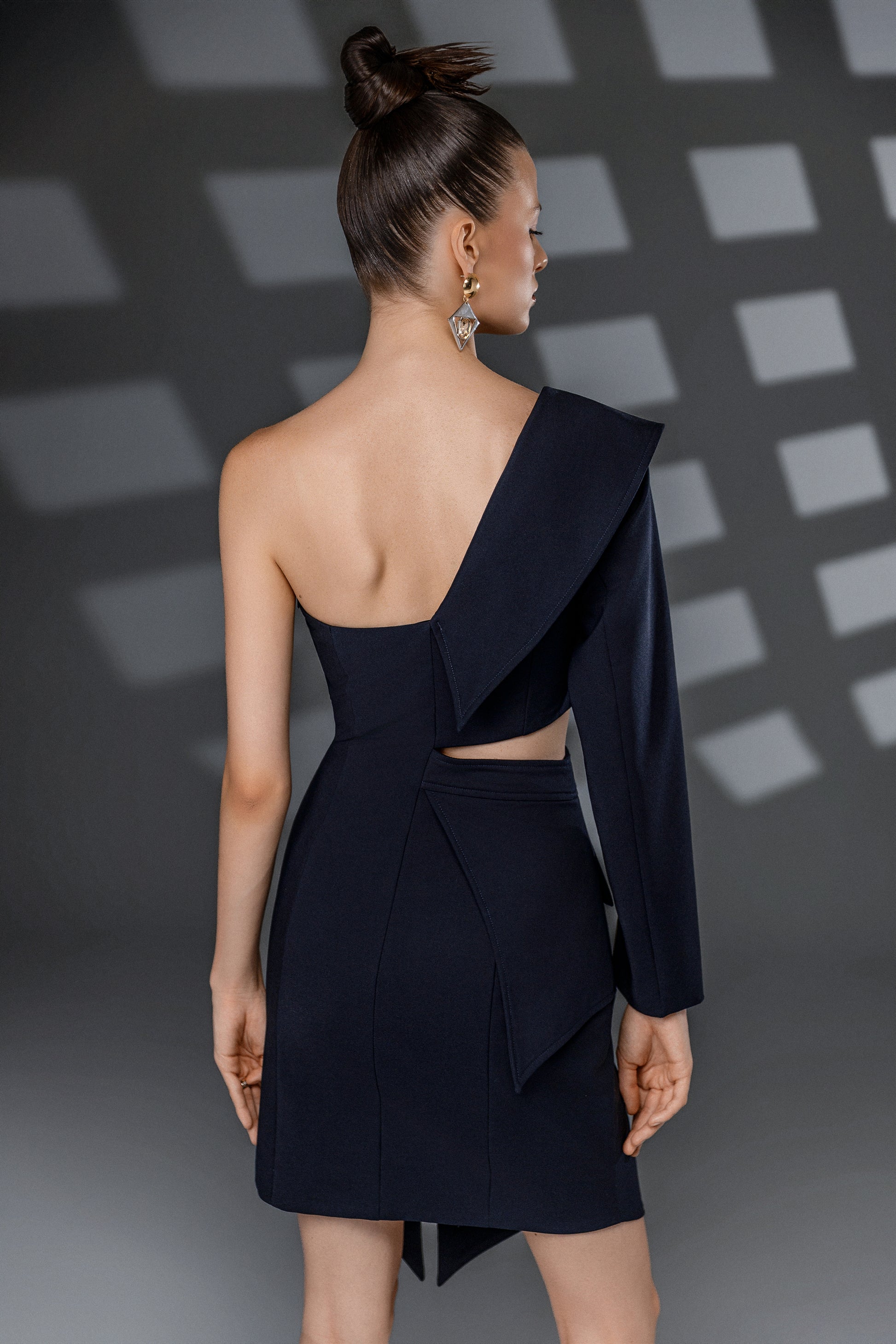 Back view of NERIS dark blue asymmetric cutout dress showing the open shoulder, layered lapel and waist cutout