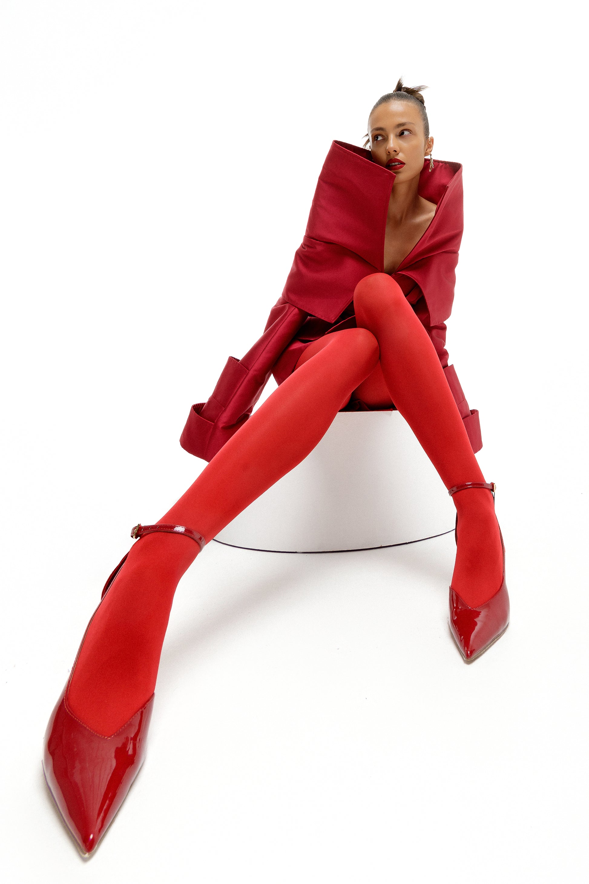 Obsidian Bloom red Mikado editorial dress in wide-angle seated portrait with sculptural high collar and elongated architectural sleeves by FlyandFall