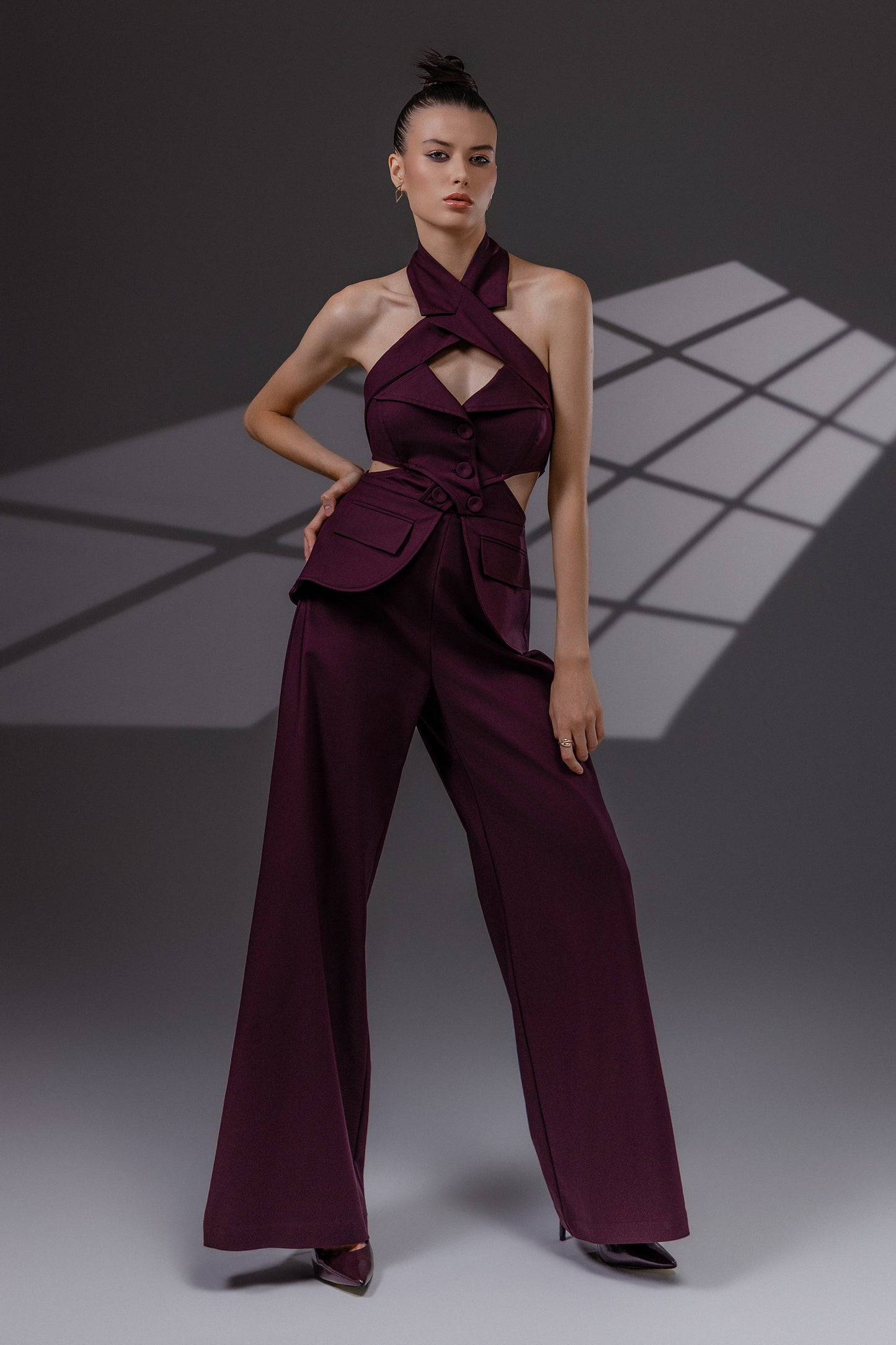 VEYRA Burgundy Crossover Halter Jumpsuit full-length front view showing the crossover halter neckline, waist cutouts, structured hip panels and wide-leg trousers.