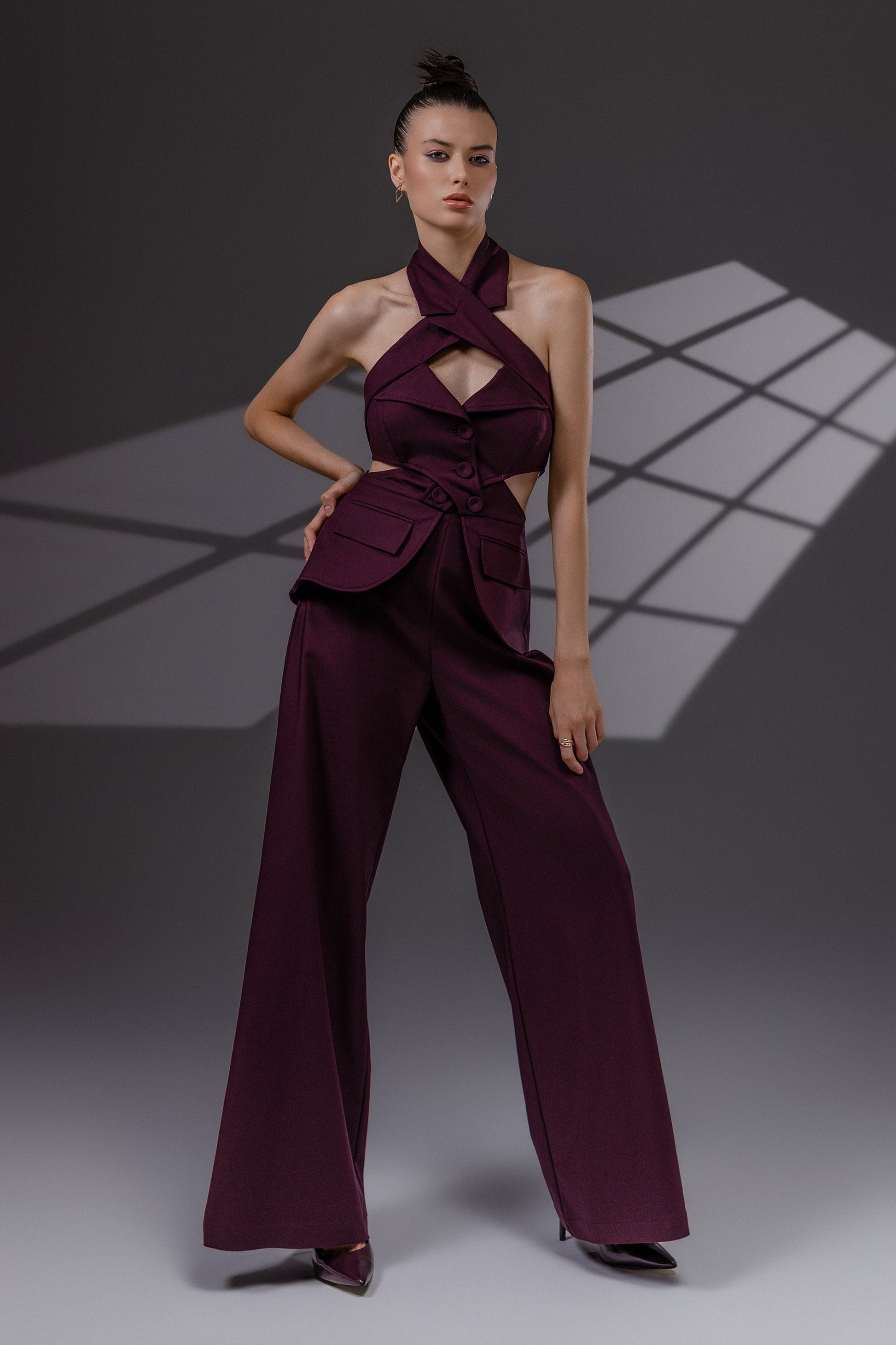 VEYRA Burgundy Crossover Halter Jumpsuit full-length front view showing the crossover halter neckline, waist cutouts, structured hip panels and wide-leg trousers.